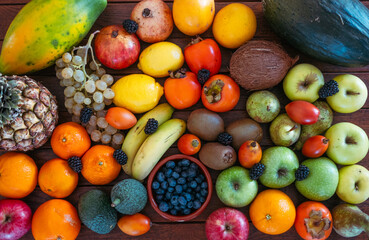 Vibrant close-up of a diverse selection of fresh tropical and seasonal fruits, including bananas, oranges, apples,  pears, grapes, avocados, blackberries, and grapefruit. Healthy eating concept
