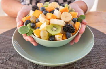 Delicious assortment of sliced fruits in a bowl for a fresh mixed fruit salad, served on a mint-green plate with a woven placemat over a rustic wooden table