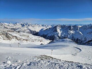 A snowy mountain range with a clear blue sky. The mountains are covered in snow and the sky is...