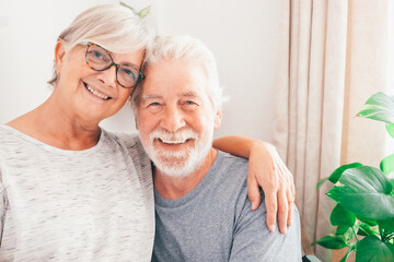 Portrait of smiling senior family couple hugging looking at camera. Happy white-haired man and woman cuddling embracing sitting at home enjoying moment of affection