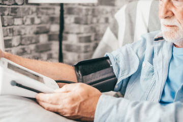 Serious senior man using medical device to measure blood pressure - senior bearded man suffering...