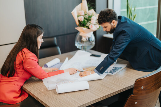 Two colleagues collaborating over blueprints in a workspace, suggesting teamwork, communication, and professional creativity in a contemporary business setting.