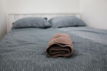 Rolled brown towel on neatly made bed with geometric patterned linens. Cozy details of the hotel's...