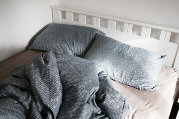 Crumpled patterned bedding and pillows in soft light on a white bed frame. The morning sunlight...