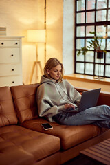 Woman Relaxing on a Sofa While Using Laptop in Cozy Home Interior