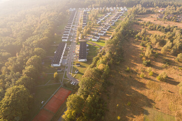 Aerial view of a modern residential development with white houses next to a forest at sunrise