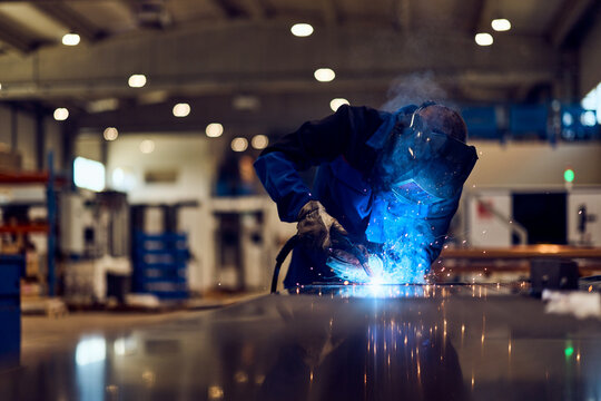 Metalworker Welding in an Industrial Workspace with Blue Sparks and Protective Gear - Powered by Adobe