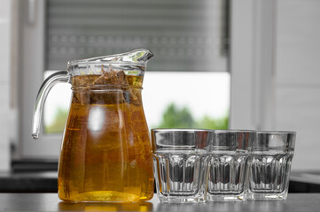 A full jug of cold drink sits on a table next to empty glasses