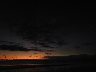 The sun setting over the ocean. A single orange glow is visible on the horizon, beneath a dark,...