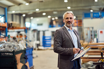 Confident Businessman Standing in Modern Industrial Warehouse Holding Paperwork