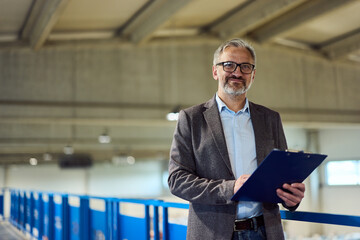 Professional Male Supervisor Holding Clipboard in Industrial Setting with Optimistic Smile
