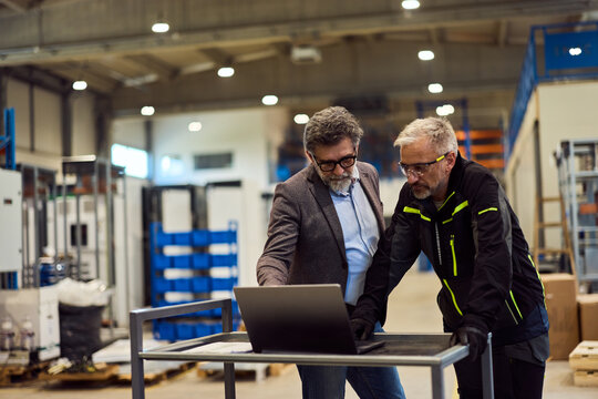 Industrial Professionals Reviewing Data on a Laptop Inside a Warehouse