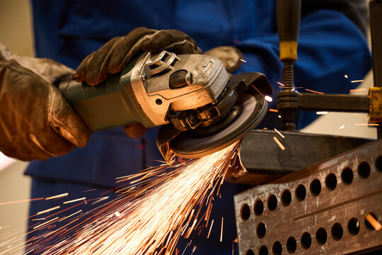 Worker Using Angle Grinder on Metal Piece with Sparks Flying in Workshop