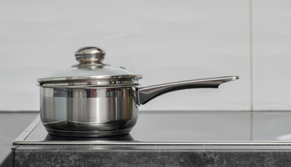 Steel saucepan with one long handle slopes on an electric hotplate, induction hob