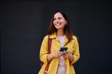Smiling Woman in Stylish Yellow Jacket Holding a Smartphone Outdoors