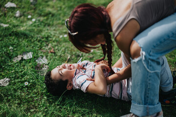 A loving mother shares a playful moment with her child outdoors, amid the grassy greenery. This...