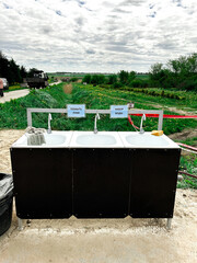 Handwashing station featuring three sinks with soap and towels, situated outdoors. Hygiene and...