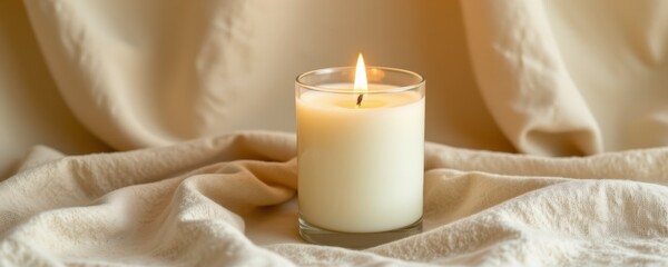 Lit White Candle in Glass on Beige Fabric