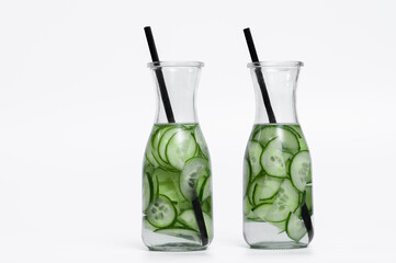 Two cucumber drinks in glass carafes with plastic straws, water with cucumber slices