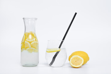 A glass of water with a slice of lemon on a light background, drinking through a straw