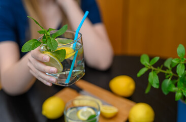 A woman drinks water with lemon and green mint.