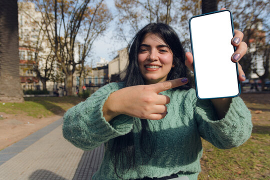 Young Venezuelan woman in the park showing her mobile screen