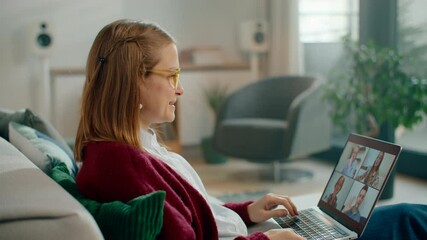 Young Woman enjoys a group online video call on laptop, smiling and talking from cozy sofa. A casual lifestyle moment of digital connection and social engagement at home. 4K medium gimbal shot - Powered by Adobe
