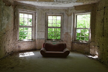 Sofa steht in marodem Abbruchhaus im Erker vor drei Sprossenfenstern