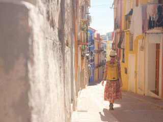 Woman in dress strolls through colorful streets of Spanish coastal town of La Vila Joiosa or Villajoyosa. sunny winter atmosphere highlights charm of Mediterranean architecture and quiet seaside life