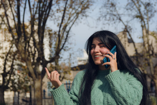Young Venezuelan woman talking on the phone and pointing in the air with her finger, smiling.
