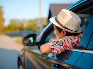 Traveler woman in red ethnic dress and hat drives car through scenic countryside of Croatia in summer. Surrounded by lush fields and forests, she enjoys peaceful and adventurous road trip