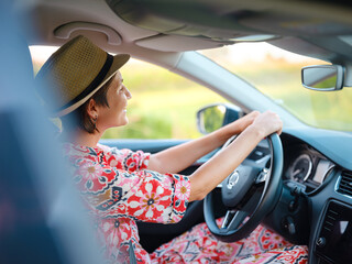 Traveler woman in red ethnic dress and hat drives car through scenic countryside of Croatia in summer. Surrounded by lush fields and forests, she enjoys peaceful and adventurous road trip