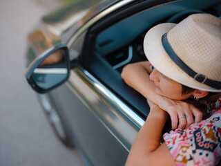 Traveler woman in red ethnic dress and hat drives car through scenic countryside of Croatia in summer. Surrounded by lush fields and forests, she enjoys peaceful and adventurous road trip