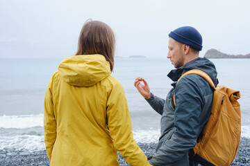 Couple enjoys Turkish coastline. Sitting on stones, watching sea waves, relaxing together, slow romantic moment near calm blue water under soft winter light.