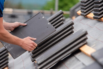 Roofer working on residential roof carefully placing and securing slate tiles with tools to ensure...