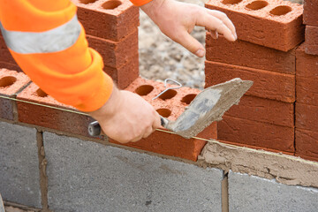 Bricklayer laying red bricks on building site