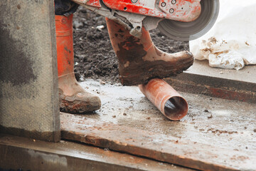 Builder cutting plastic drainage pipes at building site with power saw and diamond blade