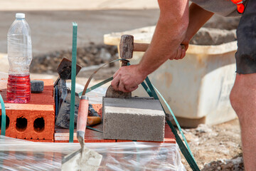 Builder cutting concrete block with chisel and hammer to right size to place it between concrete...