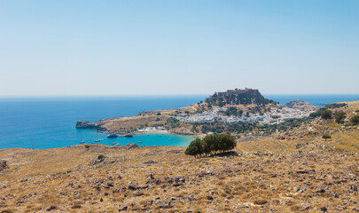 Lindos village on the island of Rhodes in Greece. Panoramic view over Lindos beach, village with whitewashed houses. The Lindos Acropolis and Temple of Athena Lindia on top of the cliff.