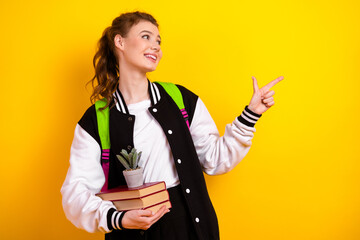 Teenage girl in casual sportswear holding book and smiling against vibrant yellow background