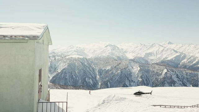 Aerial view of a black helicopter stationed on a snow-covered alpine peak in the Caucasus Mountains of Georgia during clear winter weather. Heliskiing outdoors in alps Europe concept