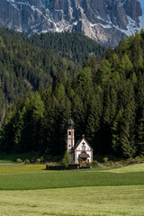 Church of St. John in Ranui in Val di Funes, Italy, with alpine meadow and Geisler Peaks in the background.