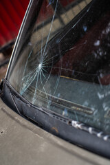 Cracked windshield glass with starburst impact damage on car seen from close-up angle outdoors
