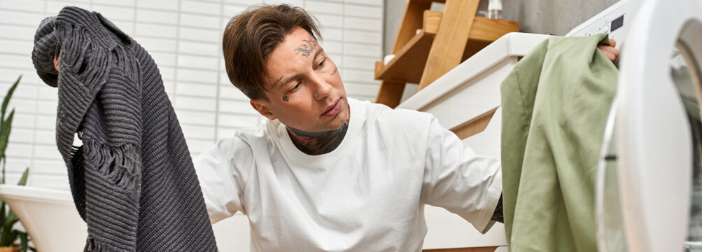 Handsome tattooed man multitasking while doing laundry in a cozy home setting