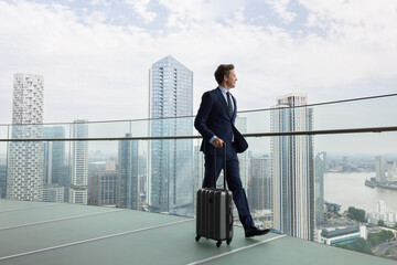 Businessman walking with Suitcase looking out at city skyline