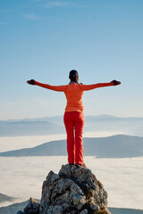 A female hiker enjoys the serene beauty of the mountain landscape, sitting on a rock at the summit, surrounded by breathtaking scenery and a sense of tranquility.