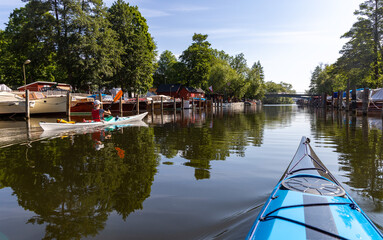 Two kayaks navigating a peaceful canal lined with boats and trees in central Stockholm, with...