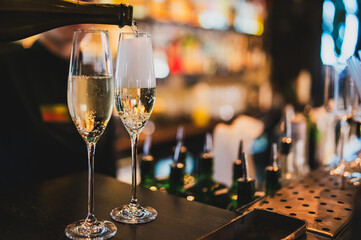 Bartender pouring drink into a tall glass with ice and chili garnish, in a blurred bar interior. Beverage preparation, nightlife concept.