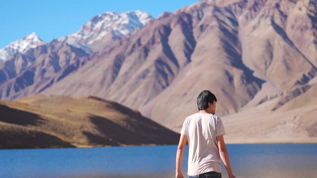 Rear View shot of Indian man walking in front of the Himalayan mountain peaks towards Chandratal Lake in Lahaul and Spiti district, Himachal Pradesh, India. Tourist in front of alpine lake in summer.