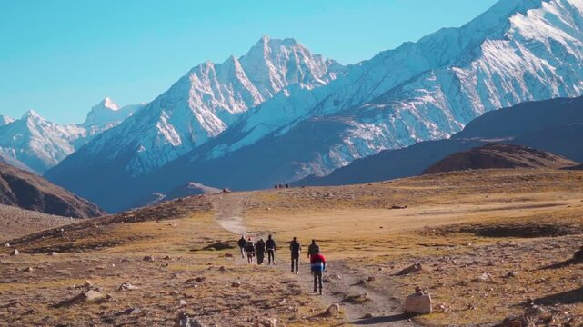 Rear view shot of group of people walking towards the snowy Himalayan mountain peak near Chandratal Lake in Spiti Valley, Himachal Pradesh, India. Group of hikers walking in front of the Himalayas.